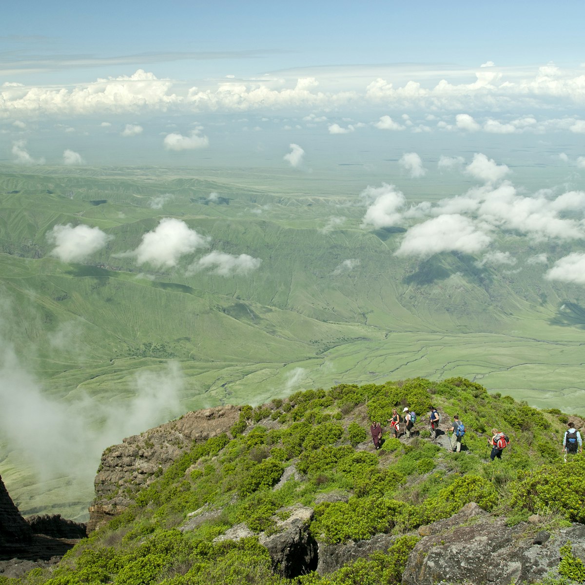 Ol Doinyo Lengai, Tanzania - January 1, 2007: A group of tourists is hiking down from the top of Ol Doinyo Lengai into the green Rift Valley, in the background the Escarpment of the Rift Valley is visible. In the foreground there is some volcanic smoke coming out of a crack.